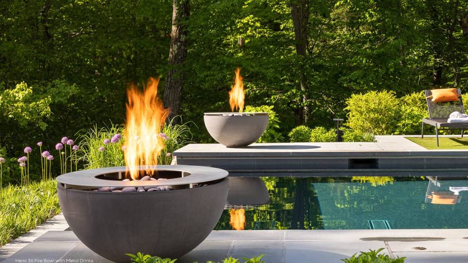 Hemi 36 fire bowl with metal drinks ring beside a contemporary outdoor swimming pool surrounded by woodland.