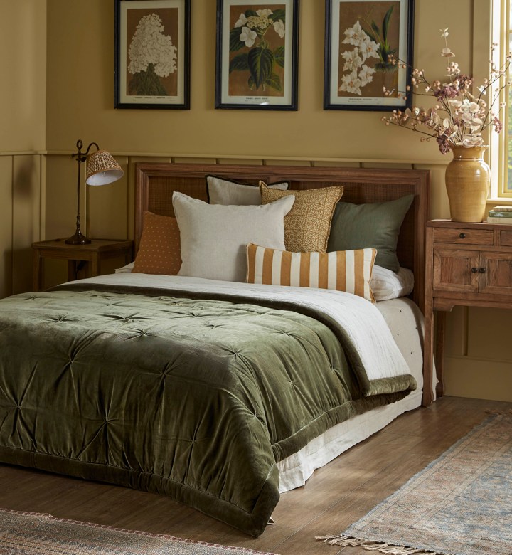 Moss-green velvet quilt layered over a bed with neutral and ochre cushions in a warm, traditional bedroom.